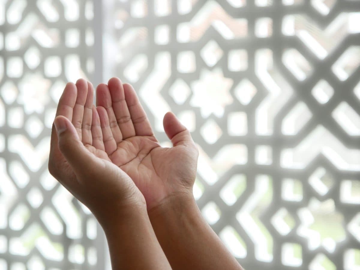 Hands open in prayer, light through a patterned screen
